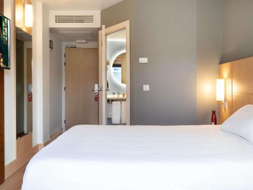 a bedroom with a large white bed and a bathroom at Ibis Madrid Alcobendas in Alcobendas