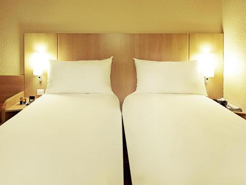 two beds in a hotel room with white pillows at ibis Criciuma in Criciúma