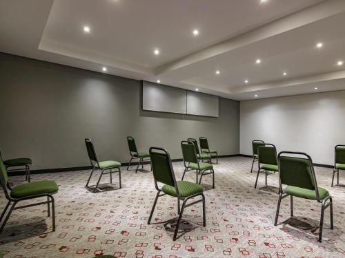 an empty room with green chairs and a projection screen at ibis Criciuma in Criciúma