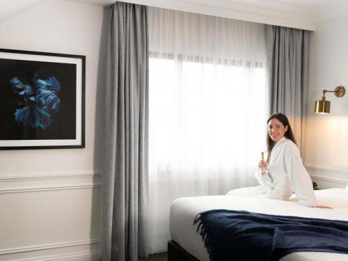 a woman sitting on a bed in a hotel room at Peppers The Hills Lodge in Castle Hill