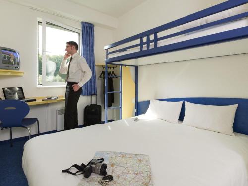 a man standing in a hotel room with a bed at ibis budget Aachen Raeren Grenze in Raeren