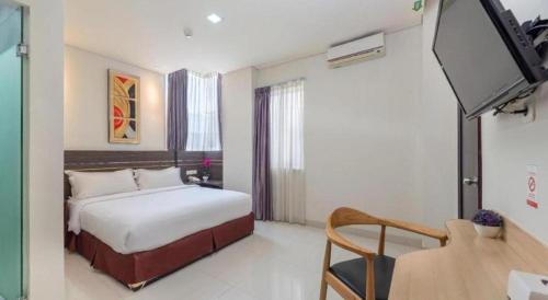 a bedroom with a bed and a desk and a tv at Life Hotel Soekarno Hatta Makassar in Makassar