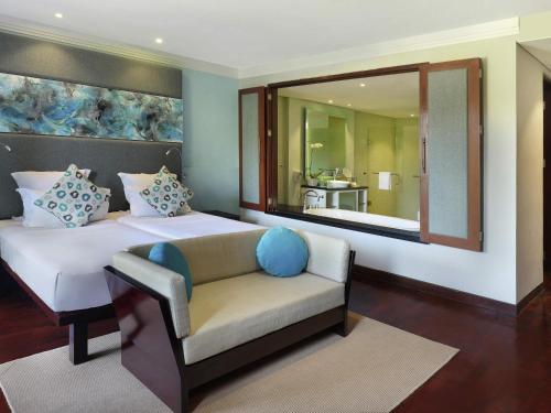 a bedroom with a bed and a chair and a mirror at Novotel Bali Nusa Dua in Nusa Dua