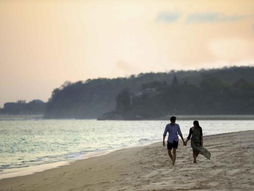 a man and woman walking on the beach at Novotel Bali Nusa Dua in Nusa Dua
