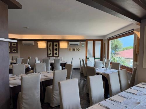 a restaurant with white tables and chairs and a large window at Hotel La Perla Del Golfo in Procchio