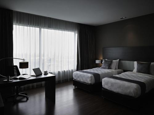 a bedroom with two beds and a desk and a window at Pullman Kuching in Kuching