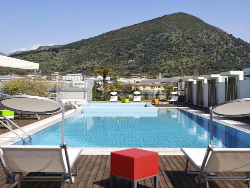 a swimming pool with chairs and a mountain in the background at Novotel Salerno Est Arechi in Salerno