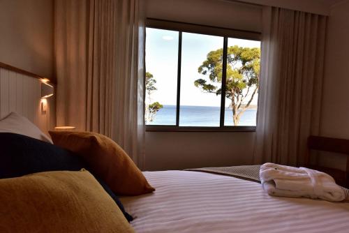 a bedroom with a bed with a view of the ocean at Lufra Beachside Hotel in Eaglehawk Neck