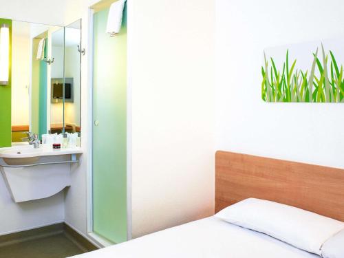 a bathroom with a bed and a sink and a mirror at ibis budget Birmingham Airport Terminal Building - NEC in Bickenhill
