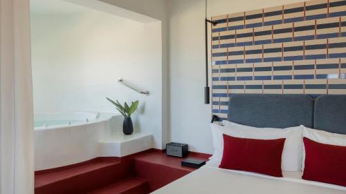 a bedroom with a bed with red pillows and a bathtub at Neema Maison Finikia Santorini in Oia