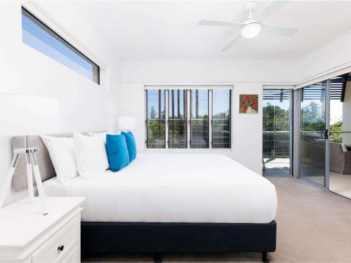 a white bedroom with a large bed with blue pillows at The Sebel Twin Waters in Twin Waters