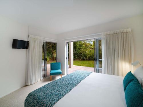 a white bedroom with a bed and a blue chair at The Sebel Twin Waters in Twin Waters