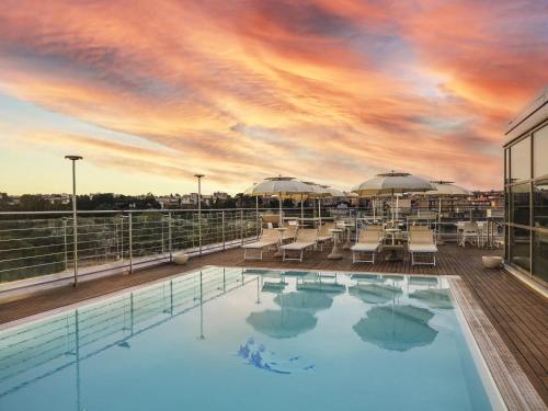 a pool on the roof of a building with a sunset at Hotel Mercure Siracusa in Siracusa