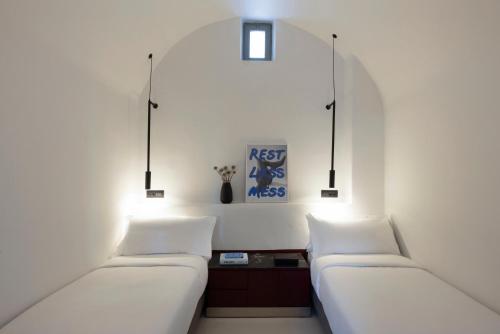 two beds in a room with white walls and lights at Neema Maison Finikia Santorini in Oia