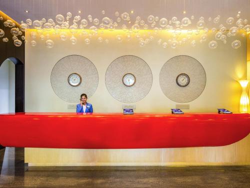 a man is standing behind a red desk with clocks at ibis Mall Avenue Dubai in Dubai