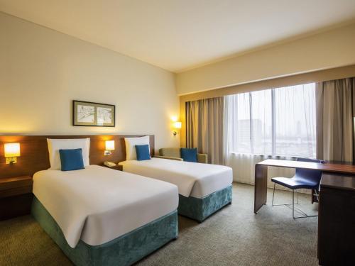 a hotel room with two beds and a desk at Novotel Deira Creekside Dubai in Dubai