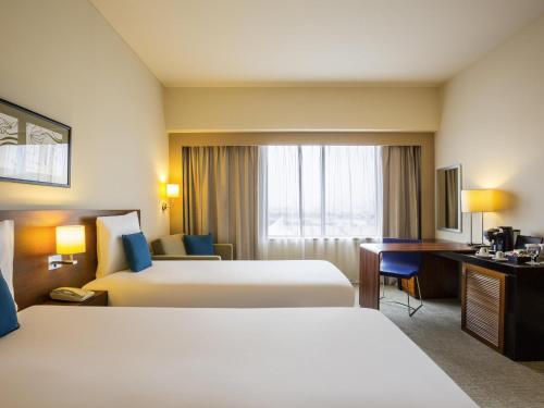 a hotel room with two beds and a desk at Novotel Deira Creekside Dubai in Dubai