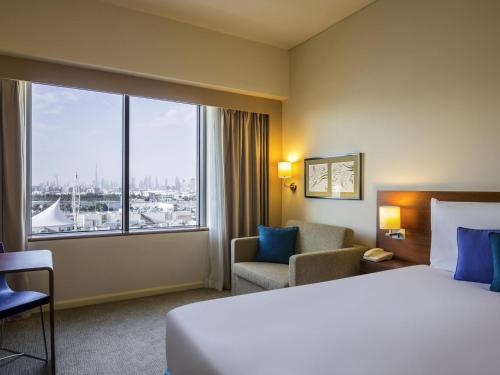 a hotel room with a bed and a chair and a large window at Novotel Deira Creekside Dubai in Dubai