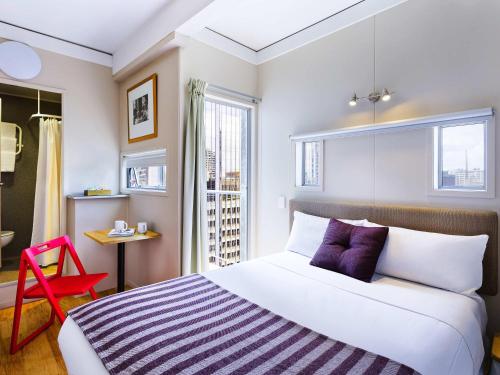 a bedroom with a large bed and a red chair at ibis budget Auckland Central in Auckland