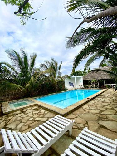 a swimming pool with two white chairs and palm trees at vii homes in Watamu