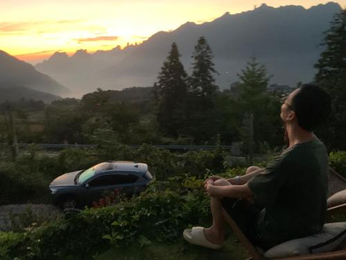 a man sitting on a bench looking out at a car at Zhangjiajie One Art Guesthouse in Zhangjiajie