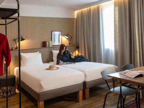 a woman sitting on a bed in a hotel room at Novotel Suites Nice Airport in Nice