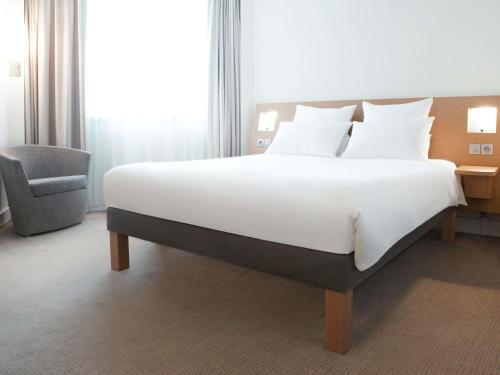 a large bed in a hotel room with a chair at Novotel Edinburgh Park in Edinburgh