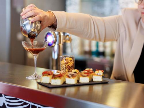 a woman pouring a glass of wine next to a tray of food at ibis Cannes Mandelieu in Mandelieu-la-Napoule