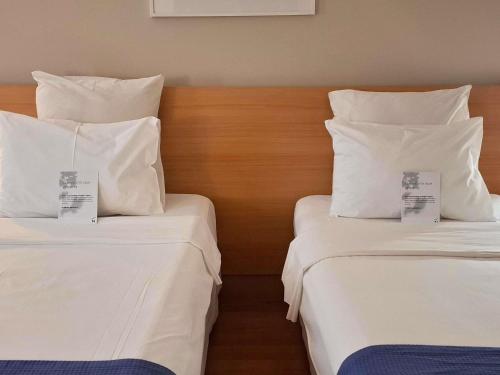 two beds in a hotel room with white sheets and pillows at Novotel RJ Santos Dumont in Rio de Janeiro