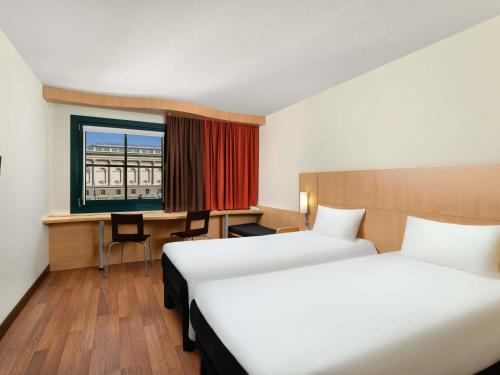 a hotel room with two beds and a desk and a window at Ibis Budapest Heroes Square in Budapest