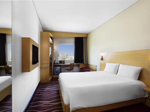a hotel room with a large white bed and a desk at ibis Muscat in Muscat