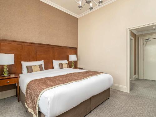 a bedroom with a large bed with a wooden headboard at Mercure Salisbury White Hart Hotel & Apartments in Salisbury