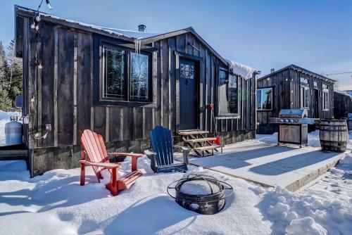 a cabin with two chairs and a table in the snow at Your Cozy Cabin Retreat in Saint-Rémi-dʼAmherst