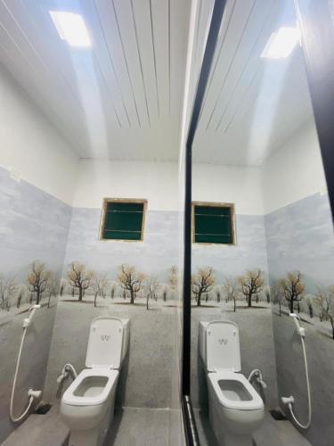 two toilets in a bathroom with trees on the wall at Rathnayaka Family & Holiday Home in Anuradhapura