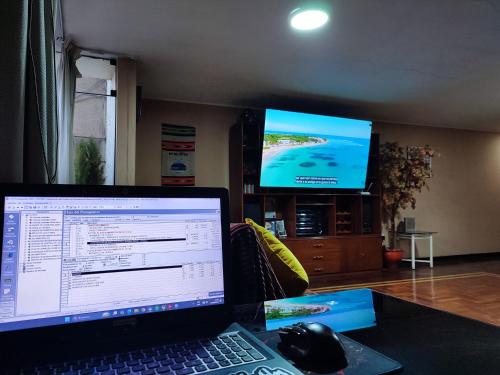 a laptop computer sitting on a desk with a television at Dpto Amplio, TV75in, Cochera, Céntrico y BBQ in Huancayo