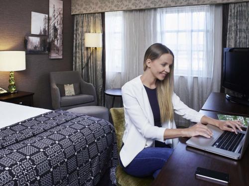 a woman sitting at a desk with a laptop in a hotel room at Mercure Exeter Southgate Hotel in Exeter