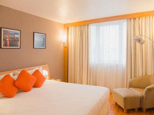 a bedroom with a bed and a chair and a window at Novotel Porto Alegre Airport in Porto Alegre