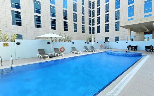 a large swimming pool with chairs and a building at Premier Inn Doha Education City in Doha