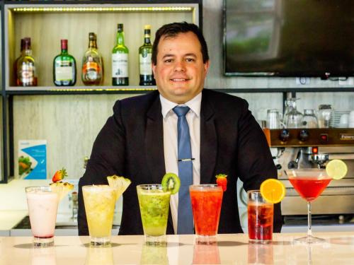 a man in a suit sitting at a table with cocktails at Novotel Porto Alegre Airport in Porto Alegre