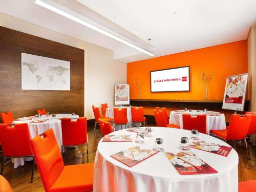 a dining room with tables and orange chairs and a screen at ibis Dubai Al Rigga in Dubai
