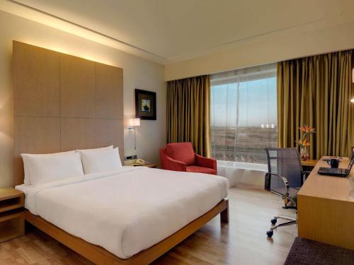 a hotel room with a bed and a desk and a window at Novotel Hyderabad Airport in Hyderabad