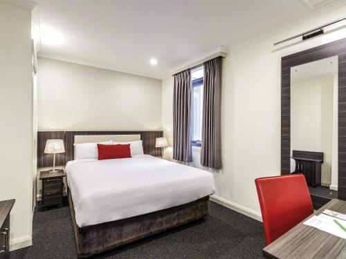 a hotel room with a bed and a red chair at ibis Styles Kingsgate Hotel in Melbourne