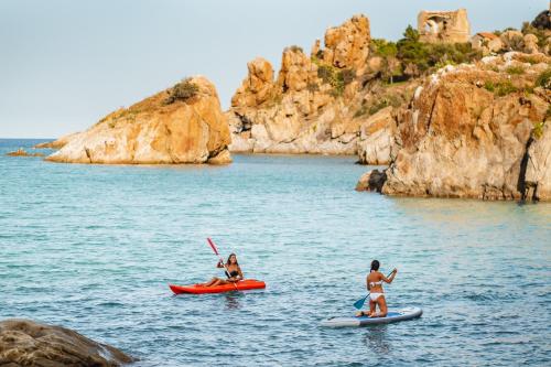 two people on kayaks in the water near a rocky shore at Le Calette Bay in Cefalù
