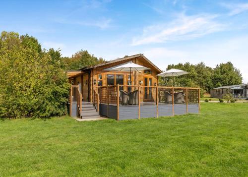 a log cabin with a deck and an umbrella at Gadlas Park Holiday Cabins in Ellesmere