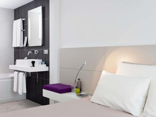 a bedroom with a white bed with a sink and a mirror at Novotel Suites Malaga Centro in Málaga