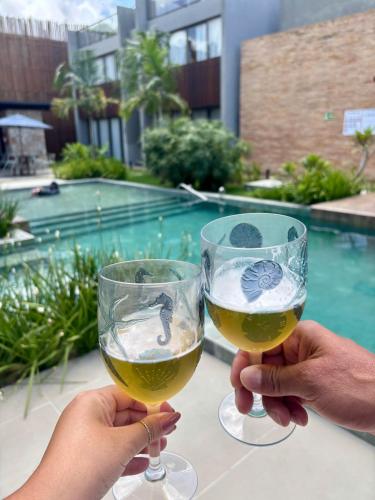 two people holding glasses of wine in front of a pool at Villa Naluri - Studio A001 no paraíso Japaratinga! in Japaratinga