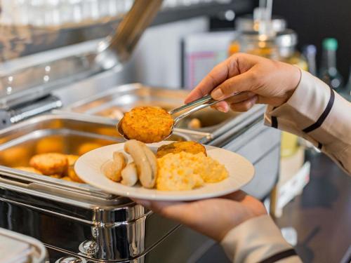 a person holding a plate of food with a spoon at Ibis Lugano Paradiso in Lugano
