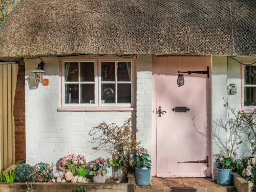 a small house with a pink door and a thatch roof at Brittons Hill Cottage in Wavehorne