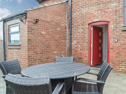 a table with chairs and a brick building with a red door at Corner Farm - Uk41369 in Carnaby