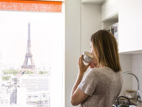 a woman drinking a cup of coffee near the eiffel tower at Aparthotel Adagio Paris Centre Tour Eiffel in Paris